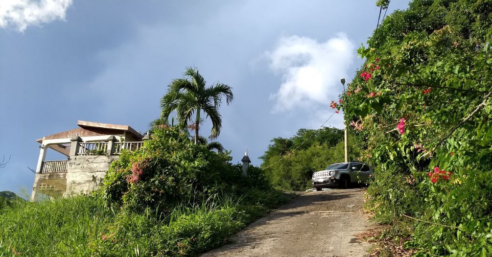 Steep road and damaged home due to Hurricane Maria