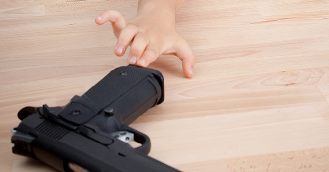 child reaching for a gun left on a wooden table