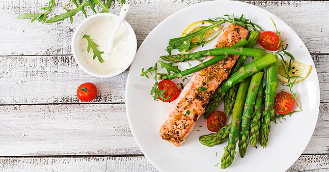 A plate of salmon and asparagus on a white wood table.