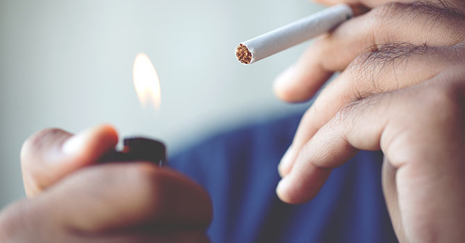 A closeup image of a person holding a cigarette up to their mouth with a lit lighter.