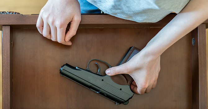 A young person reaches into a drawer for a firearm.