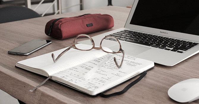 A book, glasses, phone, pencil case, and laptop on a desk.
