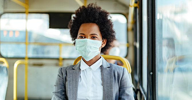 African American woman wearing a mask is sitting in a seat on a bus.