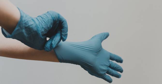 A person putting on blue hospital gloves.