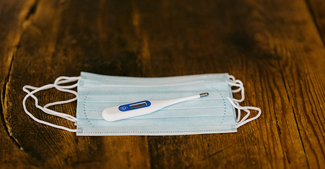 Disposable mask and a thermometer on a table.