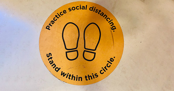 A floor sign that say to practice social distancing