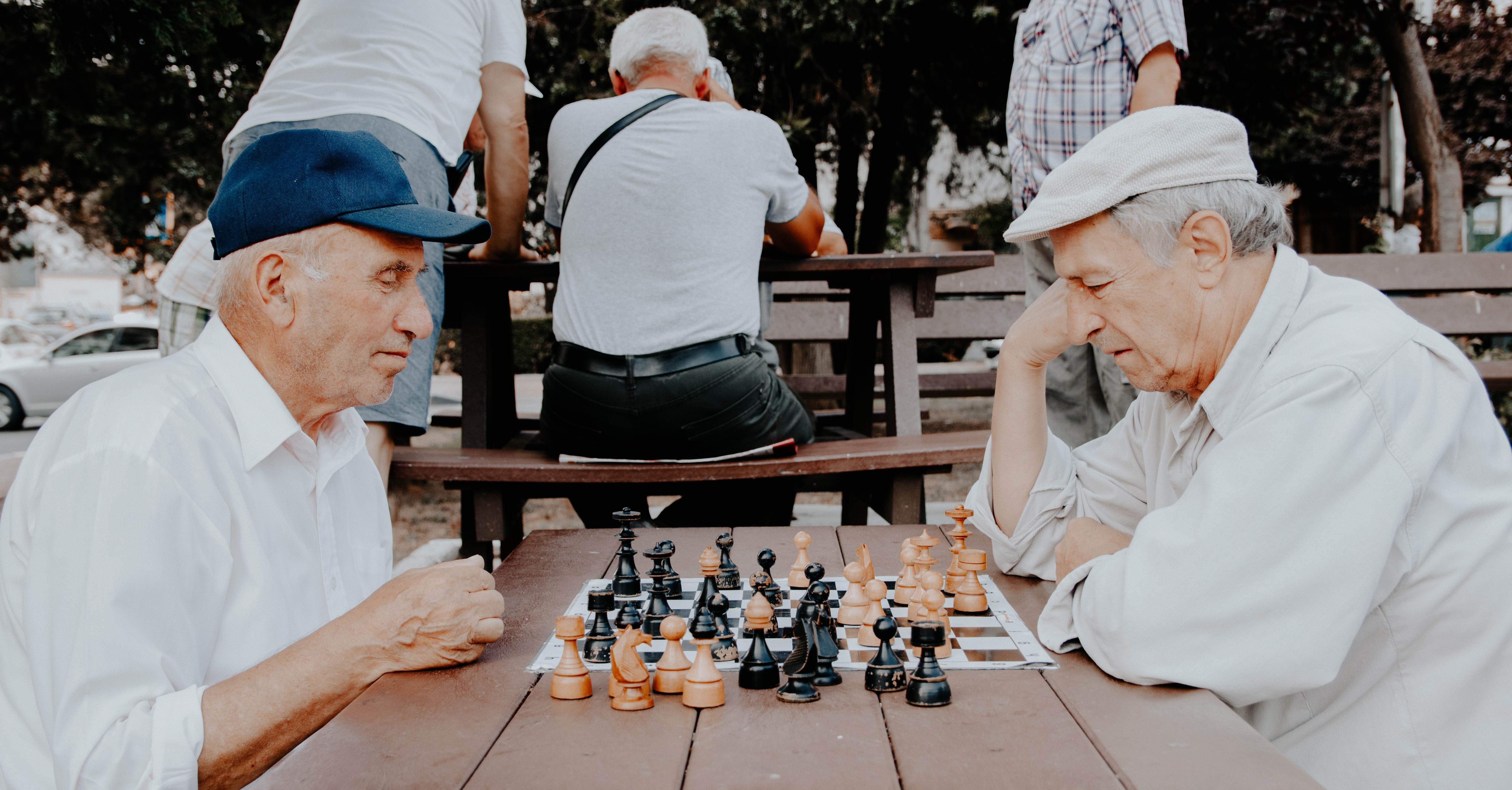 Two older adult men play chess in a park