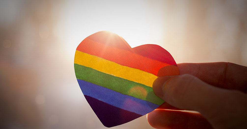 A person holding a rainbow heart sticker.
