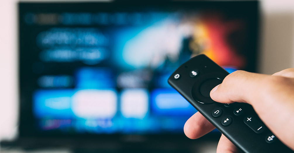 A person pointing a remote at a television.