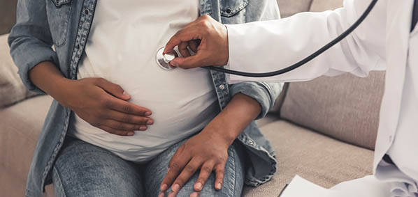 A doctor places a stethoscope on a pregnant person. 