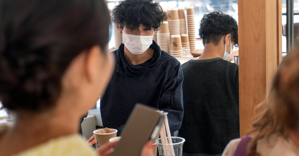 A coffee shop worker serves an unmasked customer